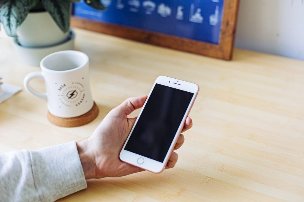 person holding iphone at brown desk